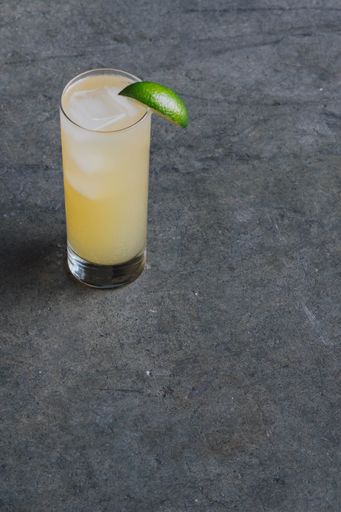 A glass of a cocktail with ice cubes and a slice of lime
