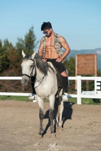 Handsome Macho Man Cowboy Riding on a Horse - Background of Sky and Mountains