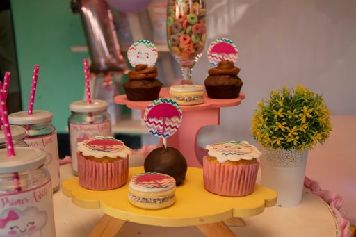 A close-up shot of different flavors cupcakes on small wooden tables and drinking glass jars with straws on a blurred background