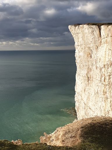 A beautiful landscape view of a rocky cliff and the sea against cloudy sky on a sunny day