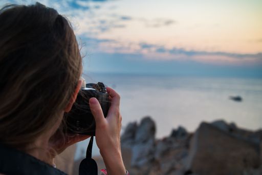 A closeup of a woman taking photos of the sea during sunset