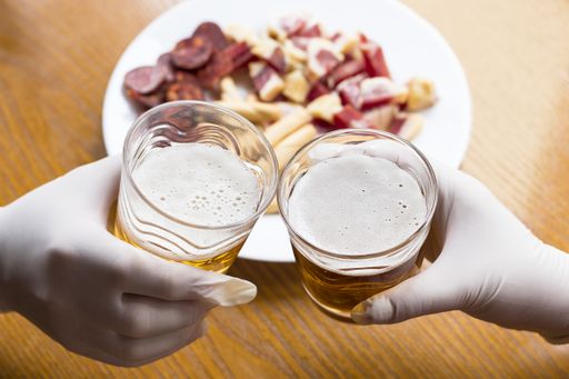A high angle shot of two people toasting with beer with plastic gloves on quarantine