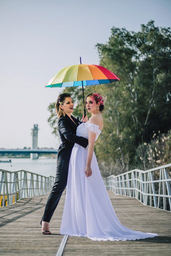 Two gorgeous young Caucasian ladies on their wedding day holding a rainbow umbrella
