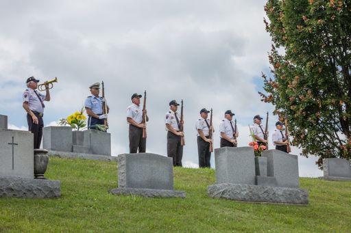 Images of military honor guardsmen at a funeral in a cemetery during the summer amidst the tombstones.