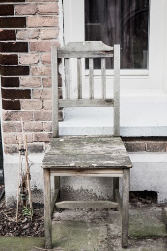 A vertical shot of an old wooden chair on a brick wall background outdoor