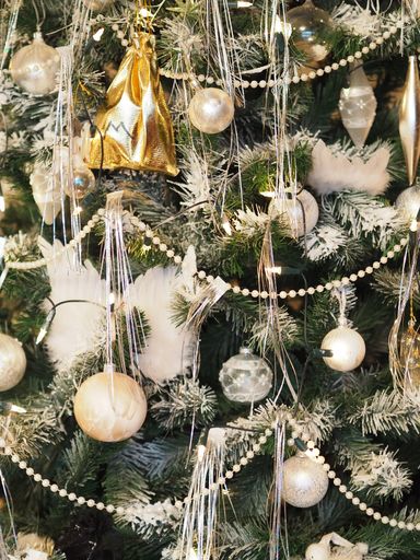 A vertical shot of a Christmas tree with decorated with white, silver and gold ornaments