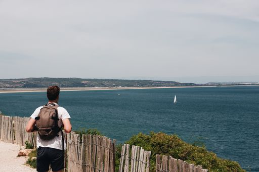 A Caucasian man with a backpack looking out into the sea under a cloudy sky
