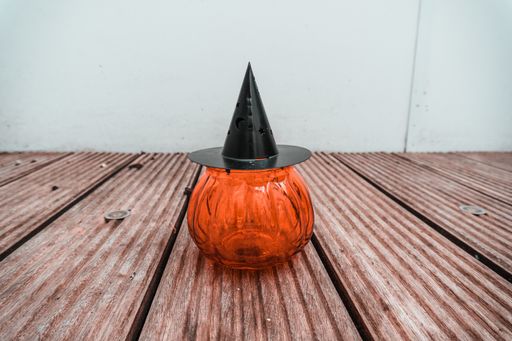 A horizontal shot of a pumpkin-shaped candle holder with a black top shaped like a hat on a wooden surface