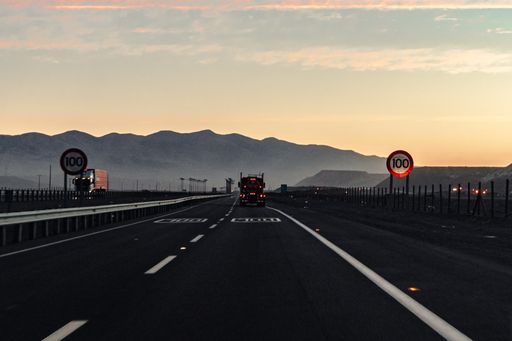 A truck driving on a highway at sunset with mountains and a cloudy sky in the background