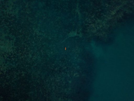 An aerial shot of the sea with a small kayak visible in the distance