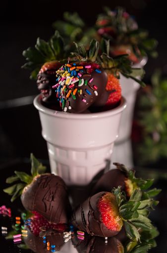 A vertical shot of chocolate covered strawberries with sprinkles in white glass cups