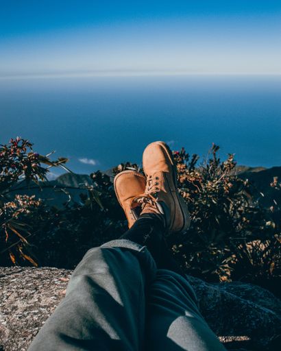 A man with leather boots relaxing on a mountain ledge while enjoying a beautiful view of nature