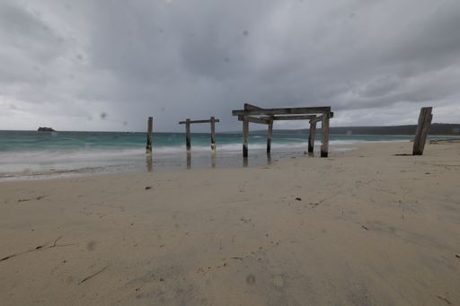 An old wooden construction of pier on a sandy beach near the ocean on a cloudy day