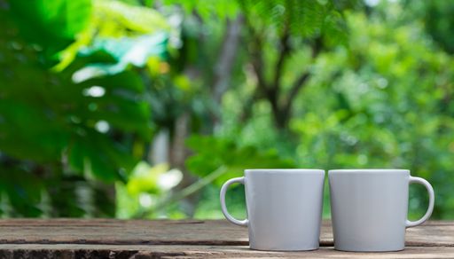 Simple two white coffe mugs placed on a wood against a blurry garden background