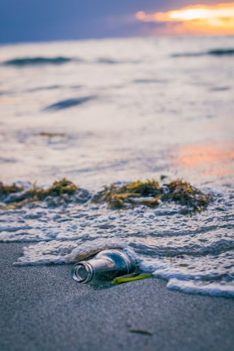 A vertical shot of a bottle on the sandy beach at sunset - pollution concept