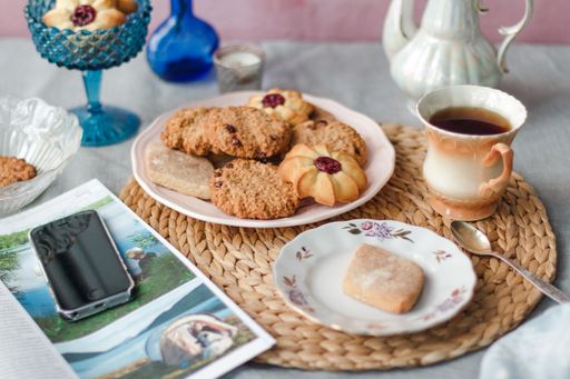 A closeup shot of fresh sweet cookies with jam and sugar powder on a white plate with a cup of tea