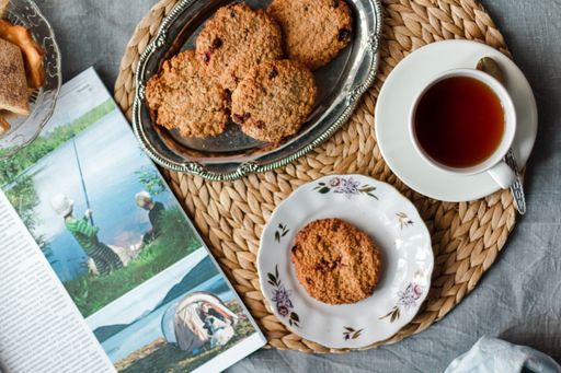 A top view of fresh baked cookies with jam on a silver tray on a table with cup of tea