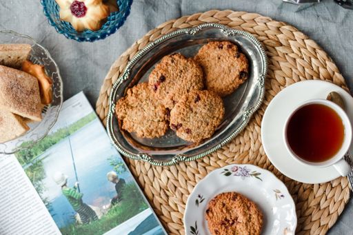 A top view of fresh baked cookies with jam on a silver tray on a table with cup of tea