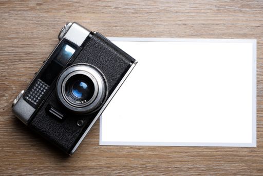 A closeup of a vintage camera and a white paper with copy space on a wooden surface