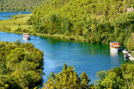 An aerial shot of a winding calm river with boats flowing through the dense forest in Krka National Park, Croatia
