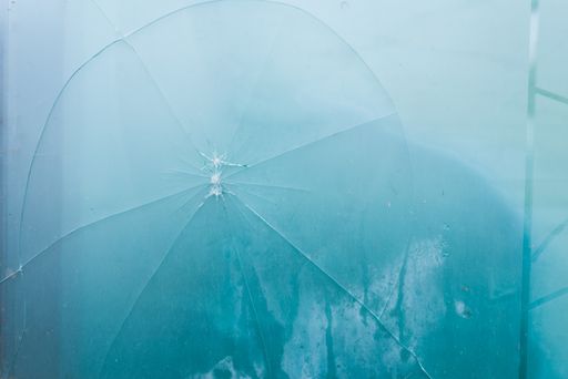 A closeup shot of a broken cracked glass with a hole on blue fog background