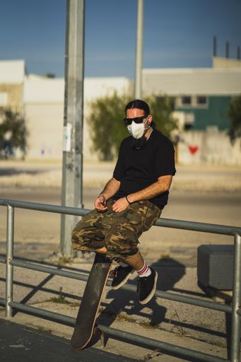 A young male sitting with a skateboard in the park wearing a medical face mask - Covid-19 concept