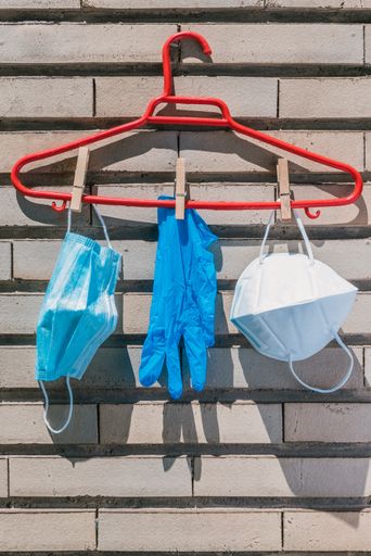 A vertical shot of medical face masks and gloves hanging on red clothes hanger on wall background
