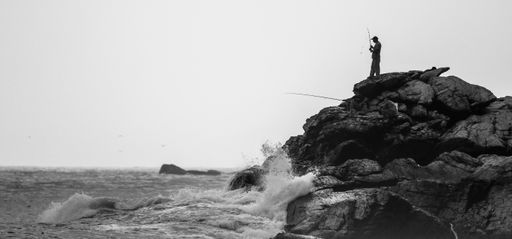 A view of a fisherman standing on top of the rocks near the sea
