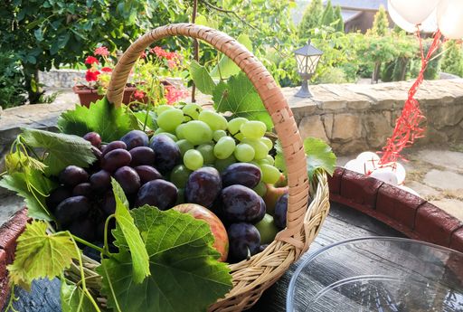 A closeup shot of a straw basket full of white grapes and plums with white balloons in the back
