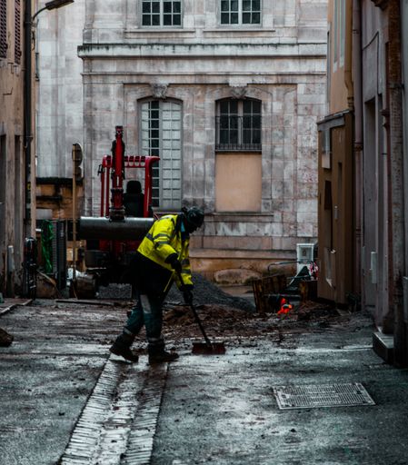 A worker male with yellow uniform cleaning in the street with old stone buildings outdoors