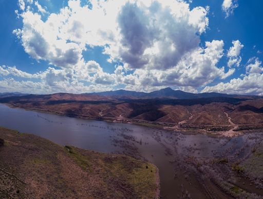 A wide-angle shot of a river in a rural area surrounded by mountains on a cloudy day