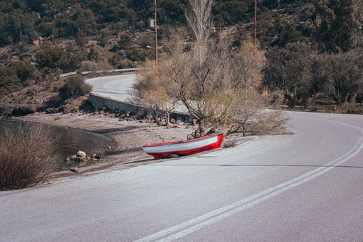 A red boat pulled out of the sea, resting on sand near the road