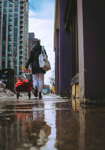 A rear view of a lady walking with a bag on wheels running errands in an urban area