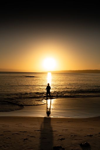 A silhouette of a man on a beach against the sunset background