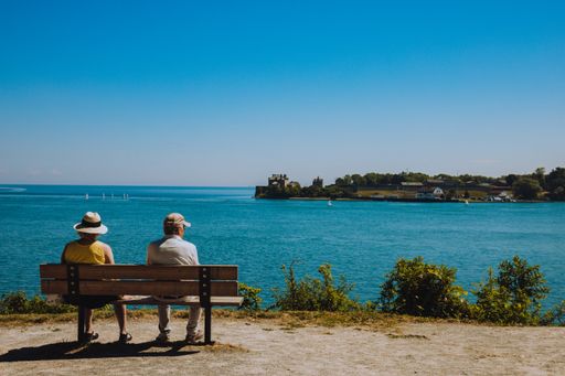 A senior couple sitting on a wooden bench in front of the sea on a blue sky background