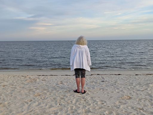 A back shot of an mature woman standing on a sandy beach, looking towards the sea against beautiful blue cloudy sky