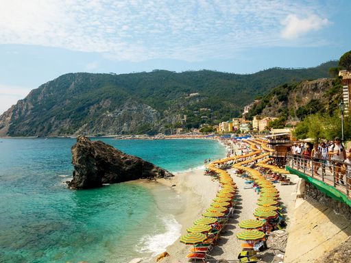 An aerial view of dozens of sun loungers and umbrellas on the sandy coast a sunny day in Cinque terre