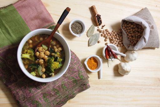 A bowl of chickpea soup with broccoli and various ingredients on a wooden table