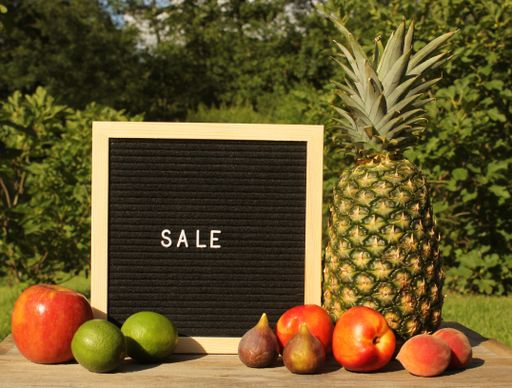 A blackboard with a sale message next to some fresh fruits in the garden.