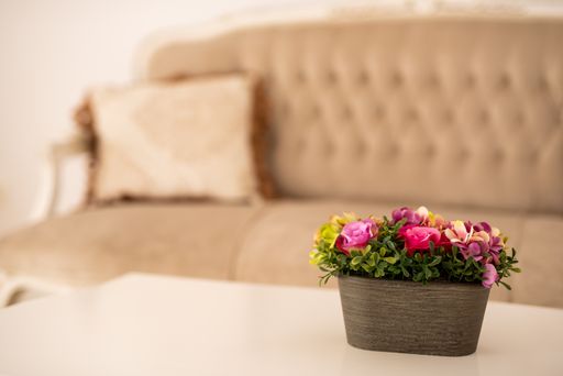 A potted pink decorative flower on a table near a sofa