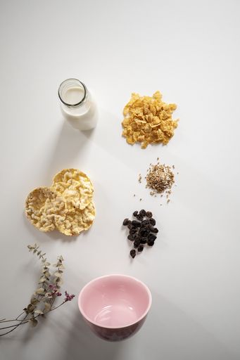 A vertical high angle shot of a pink bowl, milk bottle, and different cereals on a grey background