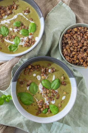 A vertical shot of bowls of lentil spinach soup with basil leaves