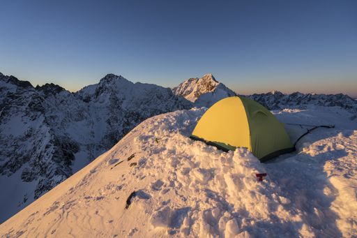 Sunset view of a yellow tent on top of snowy mountain. Winter bivi or bivouac in mountain alpine like landscape of High Tatras, Slovakia.