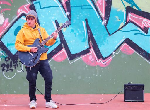 A young guy playing guitar in front of a wall with graffiti on the street of Madrid, Spain