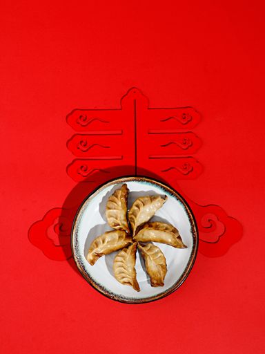 A top view of Chinese dumplings (Jiaozi) arranged in a circle in a white round plate on a red ornamented background