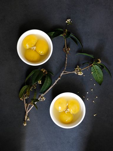 A top view of egg yolks in white bowls and a branch with white flowers in the middle on a gray surface