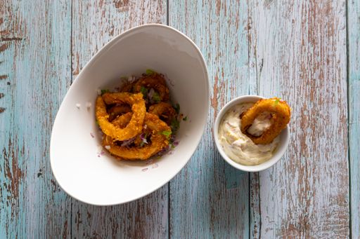 A top view of appetizing fried onions with greens and sauce in the bowls on the wooden surface