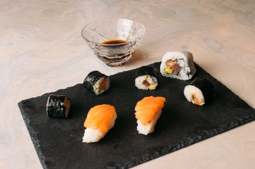 A high angle shot of rolled and cut delicious  salmon and rice sushis with soy sauce on black board