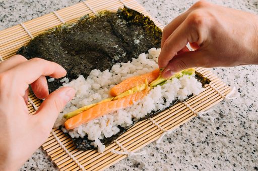 A closeup shot of a person putting the delicious sushi ingredients on the seaweed