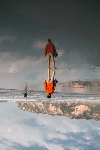 An upside-down shot of a female standing on the body of water with her reflection under the cloudy sky